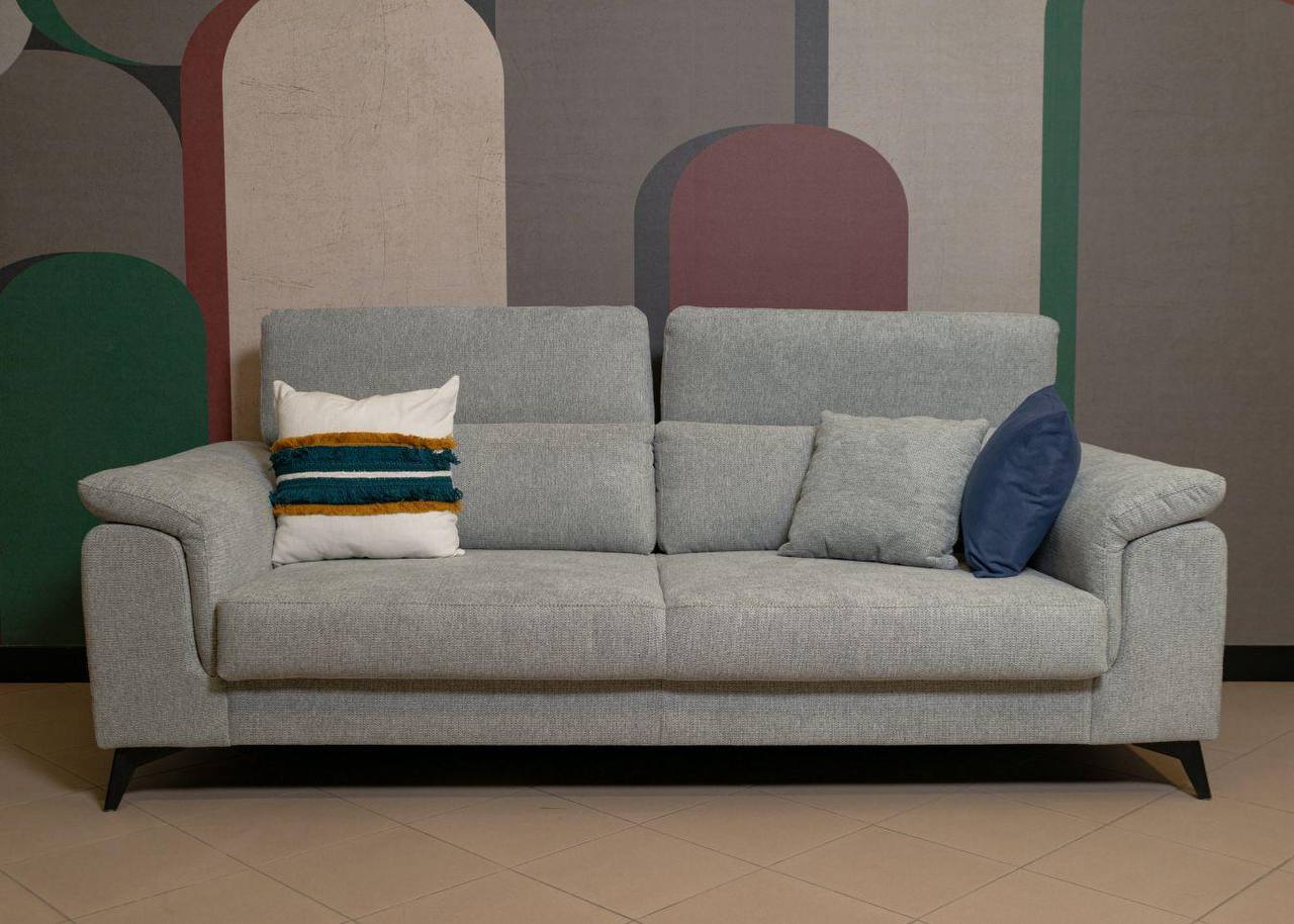 Divano grigio in tessuto con cuscini decorativi davanti a una parete con motivi ad arco