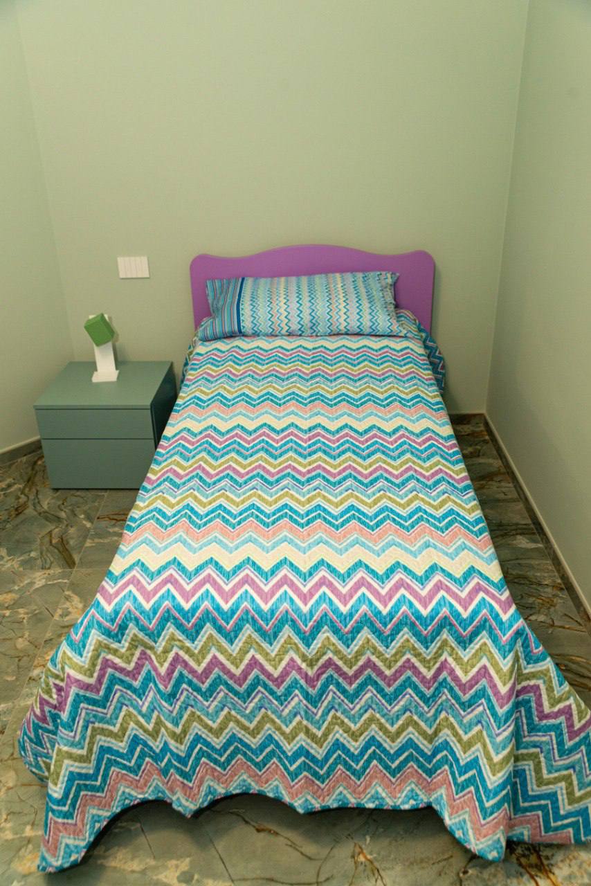 Cameretta con letto singolo lilla e comodino verde salvia